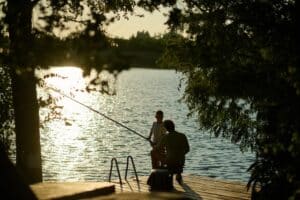 silhouette of man and child fishing on the dock of a lake 