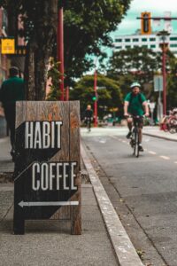 Habit Coffee's sandwich board sign on the sidewalk on a sunny day with a cyclist in the background