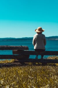 woman with a sun hat sitting on the fence along Dallas Rd Victoria, BC enjoying the view