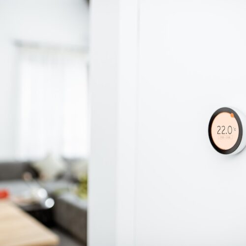 Round smart thermostat with touch screen installed on the wall indoors. Smart home heating regulation concept. View with copy space 