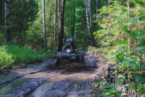 Summer Activities for adults - a trip on quad bikes on the road. Man on ATV witn safety helmets on the track in the mud participate in the cross country race in the forest on a hot summer day.