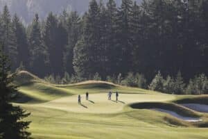View from above of four golfers playing golf on a green in the distance.