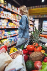 Beautiful young woman is doing shopping at the supermarket. A shopping cart full of goods in the foreground
