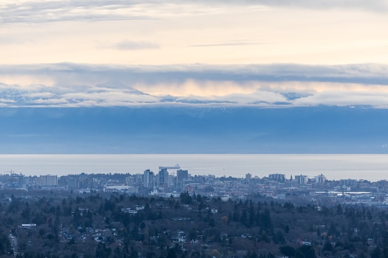 Scenic cityscape view from Mount Douglas, capturing the panoramic beauty of Victoria, Vancouver Island, with distant mountains under a cloudy sky.