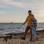 Loving couple is playing with their dog at the beach - caucasian people - people, animal, lifestyle and nature concept 