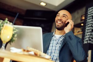 Young businessman talking on the phone with a laptop on table in cafe