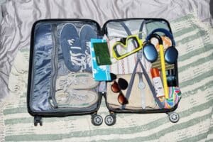 open suitcase showing summer items like light clothing, sunscreen, goggles, bathing suit sunglasses - packing, what to wear