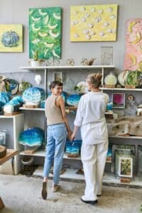 Two women, a loving lesbian couple, stand together in an art studio.